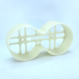 Puede incluir: Un portavasos de plástico blanco de doble cara con un patrón de rejilla. El portavasos tiene una forma redondeada y está diseñado para sostener dos vasos.