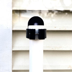 Puede incluir: Un soporte de cámara de plástico negro con un tubo de PVC blanco unido. El soporte tiene un tornillo y un anillo de plástico negro.