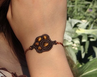 Puede incluir: Un brazalete marrón con un diseño tejido con piedras de ojo de tigre.