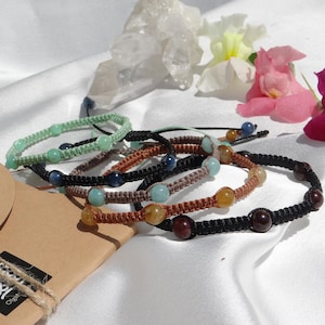 Puede incluir: Cinco pulseras trenzadas con cuentas de diferentes colores. Las pulseras están hechas con cordón negro, marrón y verde. Las cuentas son verdes, azules, marrones y rojas.