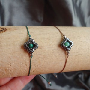May include: Two adjustable bracelets with green stone charms. The charms are silver with a four-leaf clover design. One bracelet has a green cord and the other has a brown cord.