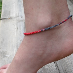 May include: A red and gray braided ankle bracelet on a person's ankle.