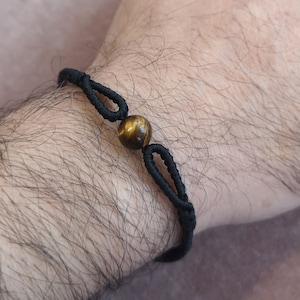 Può includere: Un braccialetto elastico nero con un solo ciondolo a forma di occhio di tigre.