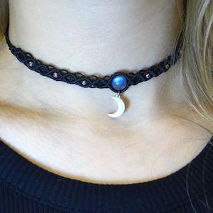 Puede incluir: Un collar gargantilla negro con un dije de media luna de plata y un colgante de piedra preciosa azul.