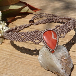 Puede incluir: Un collar de macramé marrón con un colgante de piedra jaspe roja.