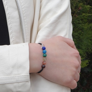 Op de afbeelding: Een zwarte armband met zeven gekleurde edelsteen kralen. De kralen zijn blauw, blauwgroen, groen, oranje, bruin, rood en helder.