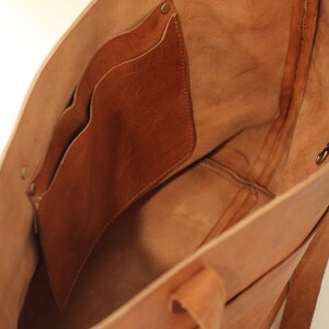 Puede incluir: Un bolso tote de cuero marr&oacute;n con un bolsillo interior grande y dos bolsillos m&aacute;s peque&ntilde;os. El bolso tiene una cremallera superior y dos asas largas.