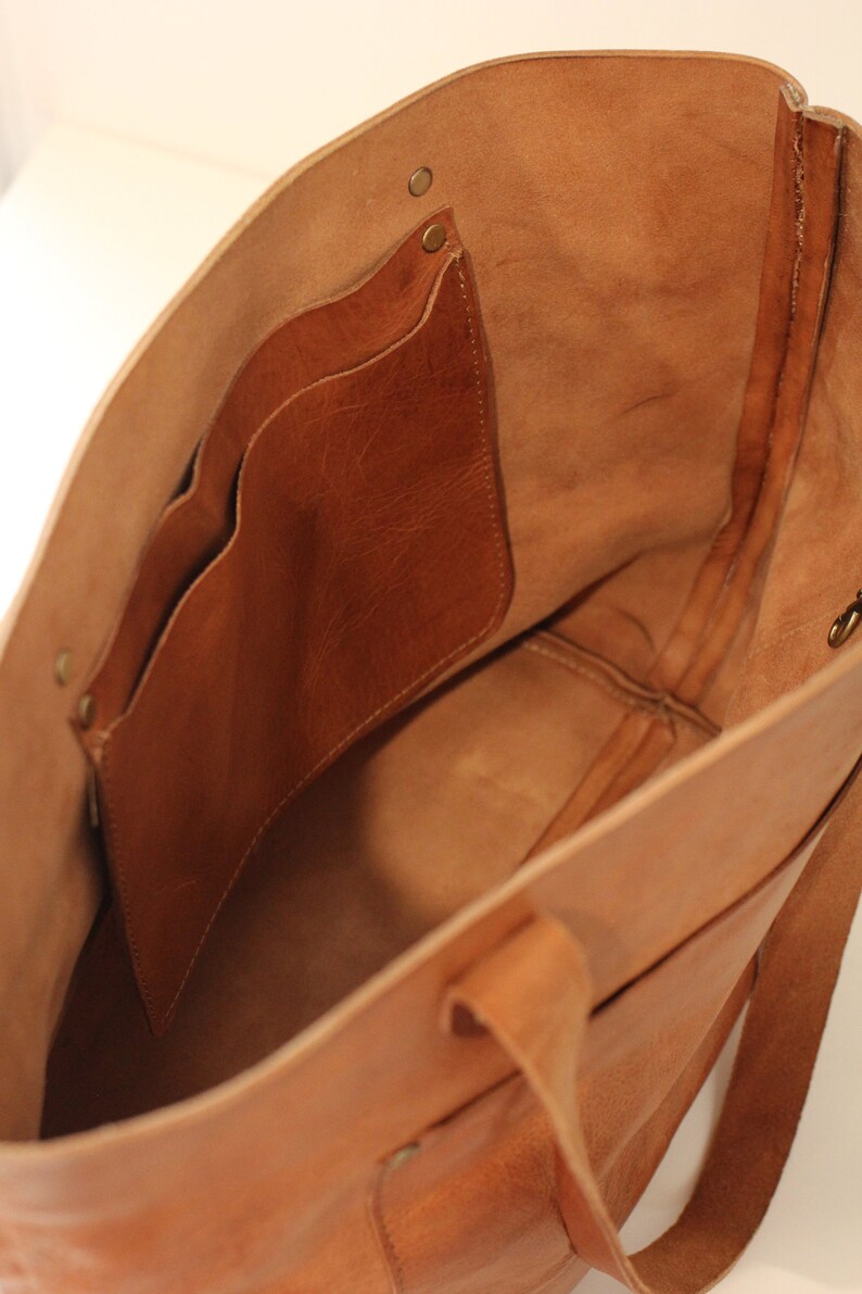 Puede incluir: Un bolso tote de cuero marr&oacute;n con un bolsillo interior grande y dos bolsillos m&aacute;s peque&ntilde;os. El bolso tiene una cremallera superior y dos asas largas.