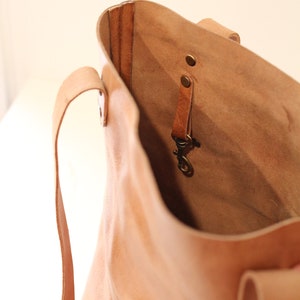 Puede incluir: Un bolso tote de cuero marr&oacute;n claro con un interior espacioso. El bolso tiene dos asas y una peque&ntilde;a correa con un cierre en el interior. El cuero tiene un aspecto natural y texturizado, y el bolso parece hecho a mano.