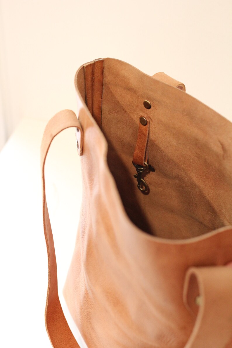 Puede incluir: Un bolso tote de cuero marr&oacute;n claro con un interior espacioso. El bolso tiene dos asas y una peque&ntilde;a correa con un cierre en el interior. El cuero tiene un aspecto natural y texturizado, y el bolso parece hecho a mano.