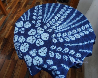 Könnte beinhalten: Ein runder, indigoblauer Tischläufer mit weißem Batikmuster. Das Design zeigt ein zentrales Blumenmotiv, das von radialen Linien und kleineren Blumenformen umgeben ist. Das Tuch ist über einem runden Tisch drapiert.