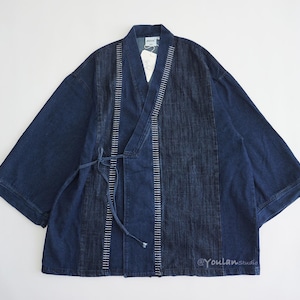 Könnte beinhalten: Dunkelblaue Jeans-Kimono-Jacke mit Wickelverschluss und weiten Ärmeln. Die Jacke hat vertikale Bahnen mit weißen Nähten und einen Bindverschluss in der Taille. Das Etikett lautet "@youlanstudio".