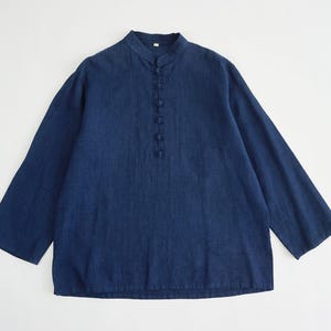 May include: A navy blue shirt with a mandarin collar and long sleeves. It features a button-down placket and is made from a textured fabric. The shirt has a relaxed fit and is a solid colour. The sleeves are long and loose.