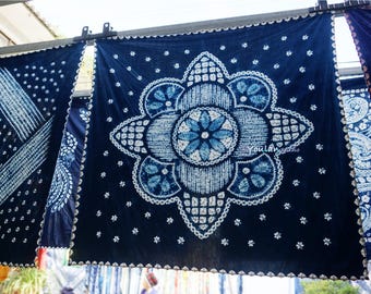 Könnte beinhalten: Indigogefärbte Stoffbahnen mit aufwendigen weißen Mustern. Das zentrale Panel zeigt ein großes Blumendesign, umgeben von kleineren floralen Motiven. Der Stoff hängt und zeigt die detaillierte Handwerkskunst und Textilkunst.