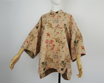 Könnte beinhalten: Beige Oberteil mit floralem Druck, Stehkragen und weiten Ärmeln. Das Oberteil hat ein Muster aus roten, rosa und grünen Blumen mit braunen Stielen und Blättern. Das Kleidungsstück hat einen einzigartigen, asymmetrischen Saum.