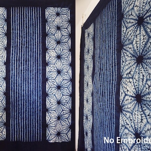 Op de afbeelding: Een blauwe en witte indigo-geverfde stof met een geometrisch patroon. De stof hangt aan een muur en heeft een label met de tekst "Geen borduurwerk".