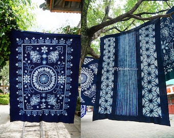May include: Indigo blue fabric panels with intricate white designs, including fish, flowers, and geometric patterns, hanging on a clothesline outdoors.