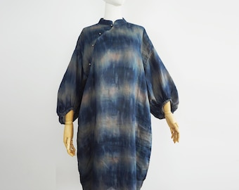 Könnte beinhalten: Blau-beiges Batik-Kleid mit langen, voluminösen Ärmeln. Das Kleid hat einen Stehkragen und einen Knopfverschluss. Der Stoff hat ein weiches, fließendes Aussehen, und das Kleid wird auf einer Schaufensterpuppe präsentiert.