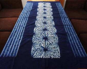 Könnte beinhalten: Dunkelblaues Textil mit weißem Muster. Der Mittelteil weist ein sich wiederholendes geometrisches Muster auf, während die Ränder vertikale Streifen aufweisen. Das Textil wird auf einer Holzoberfläche mit den Worten "Youlan Studio" präsentiert.