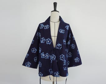 Könnte beinhalten: Marineblaue Jacke im Kimono-Stil mit einem Blumenmuster in hellblauen Farbtönen. Die Jacke hat weite Ärmel und einen Bindverschluss in der Taille. Das Kleidungsstück wird auf einer Schaufensterpuppe präsentiert.