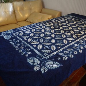 May include: A dark blue tablecloth with a white floral pattern. The rectangular cloth is draped over a table, showcasing a repeating design of oval shapes and leaf-like motifs. The tablecloth is made of fabric.