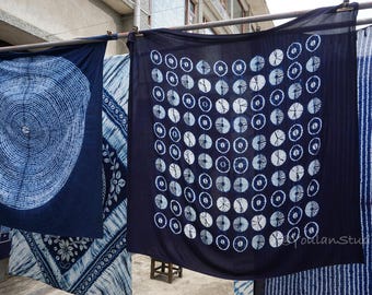Könnte beinhalten: Im Freien hängende, indigogefärbte Stoffbahnen. Die Bahnen weisen verschiedene Muster auf, darunter konzentrische Kreise, ein Baumringdesign und Streifen. Der Stoff ist ein tiefes Marineblau mit weißen Designs.