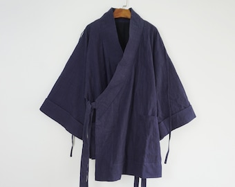Könnte beinhalten: Eine dunkelblaue Wickeljacke mit weiten Dreiviertelärmeln mit umgeschlagenen Manschetten, einem V-Ausschnitt und langen Stoffbändern an der Seite zum Binden. Das Kleidungsstück hat eine strukturierte Oberfläche und hängt an einem Holzkleiderbügel.