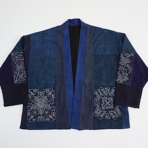 Peut inclure: Une veste en patchwork bleu avec des broderies blanches. La veste est faite de différentes nuances de tissu bleu et a un style japonais traditionnel.