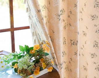 May include: Beige floral curtains with a delicate pattern of white and black botanical elements. The curtains are partially drawn, revealing a window and a bouquet of yellow flowers. Tassels adorn the edge of the curtain.