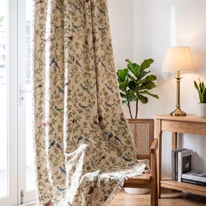 Op de afbeelding: Beige gordijn met een herhalend patroon van vogels en bladeren in blauwe, rode en groene tinten. Het gordijn heeft een franjebies en hangt voor een raam. De tekst "LucyHomeDesign" is zichtbaar.