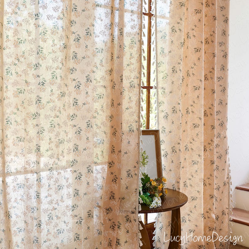 Op de afbeelding: Transparante beige bloemengordijnen. De gordijnen hebben een delicaat patroon van kleine bloemen in roze, groen en beige. Ze hangen voor een raam en laten licht door. De tekst "LucyHomeDesign" is zichtbaar.