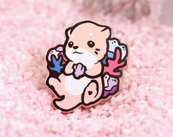 May include: A pink enamel pin featuring a cartoon otter holding coral and sea life. The otter is surrounded by pink, blue, and purple coral.