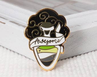 May include: A gold-colored enamel pin featuring a potion bottle with a black and white swirl design. The bottle is filled with green, white, and gray liquid. A white banner with the word "Awesome" is wrapped around the bottle.