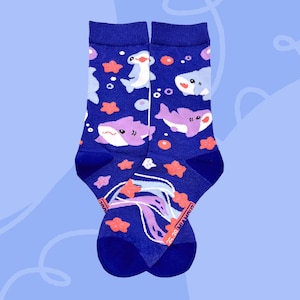 Pode incluir: Um par de meias azul marinho com um design subaquático caprichoso. As meias apresentam tubarões de desenho animado, estrelas do mar e outras criaturas marinhas em tons de roxo, branco e laranja. Um acessório divertido e colorido.