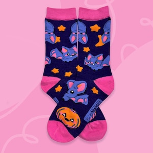 May include: Novelty socks featuring a dark blue background adorned with cartoon bats, stars, and pumpkins. The toes and cuffs are bright pink. These socks are a fun and colourful accessory.
