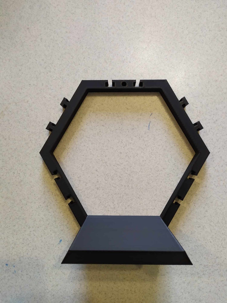 Puede incluir: Un soporte hexagonal negro con una base plana. El soporte tiene una serie de peque&ntilde;os agujeros alrededor del borde superior.
