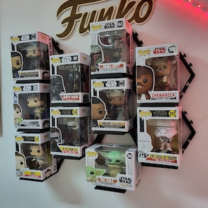 Puede incluir: Una estanter&iacute;a de pared en blanco y negro con un letrero de madera que dice "Funko" y una colecci&oacute;n de figuras Pop! de Star Wars. Las figuras incluyen Boba Fett, Darth Vader, Chewbacca, Rey, Kylo Ren y The Child.