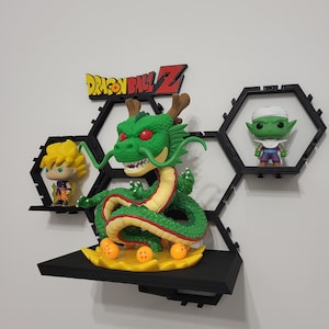 May include: A black hexagonal shelf with a green dragon figurine, a yellow and orange Dragon Ball Z logo, and two small figurines. The dragon is holding a red ball in its mouth and has red eyes. The figurines are in black hexagonal frames.