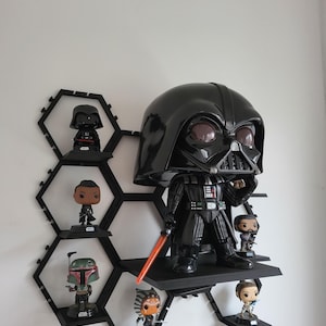 Könnte beinhalten: Ein schwarzes sechseckiges Regal mit sechs Ablagen, auf denen Star Wars Pop-Figuren ausgestellt sind. Zu den Figuren gehören Darth Vader, Boba Fett, Ahsoka Tano und andere. Die größte Figur ist eine große Darth Vader Pop-Figur.