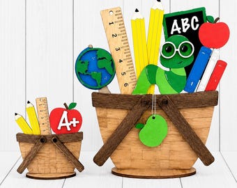 May include: Two wooden baskets filled with school-themed cutouts. The larger basket contains a globe, a 6-inch ruler, two yellow pencils, a green worm with glasses, a chalkboard with 'ABC', and a red apple. The smaller basket holds two pencils, a 4-inch ruler, and a red apple with 'A+'.