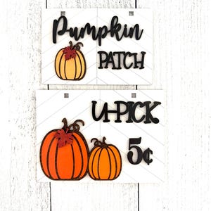May include: Two wooden signs with a pumpkin patch theme. The top sign says "Pumpkin Patch" with a single orange pumpkin with a brown stem and a red leaf. The bottom sign says "U-Pick 5&cent;" with two orange pumpkins with brown stems and red leaves.