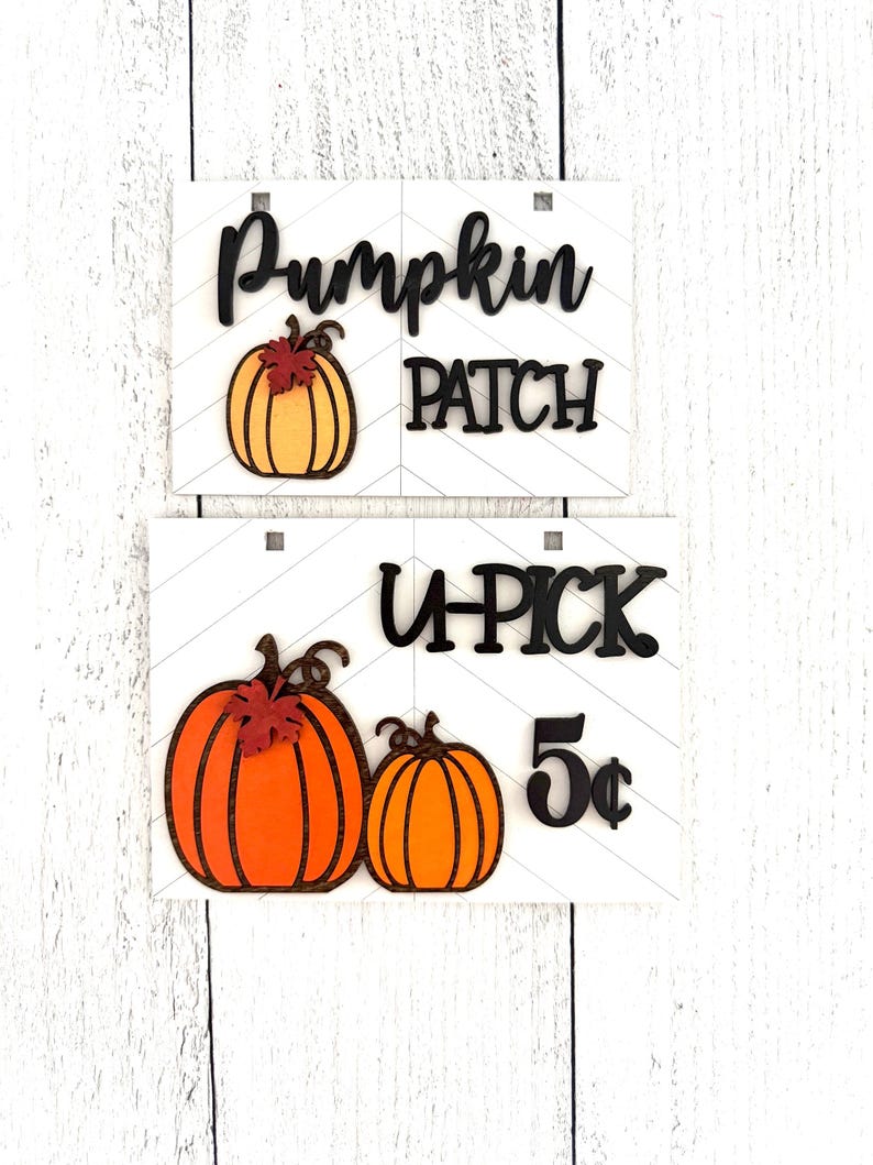 May include: Two wooden signs with a pumpkin patch theme. The top sign says "Pumpkin Patch" with a single orange pumpkin with a brown stem and a red leaf. The bottom sign says "U-Pick 5&cent;" with two orange pumpkins with brown stems and red leaves.