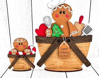 May include: Two wooden basket decorations featuring gingerbread characters. The larger basket holds a gingerbread baker with a chef hat, whisk, red mitten, rolling pin, spatula, and green tree cookie. A tag reads Sweet Holiday Wishes.