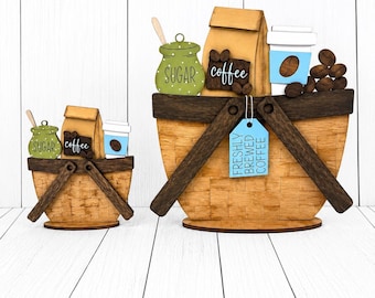 May include: Two wooden basket-shaped tiered tray decorations featuring a tan woven pattern, dark brown handles, and coffee-themed accents including a green sugar jar, a tan coffee bag, a blue coffee cup, and a blue tag reading FRESHLY BREWED COFFEE.