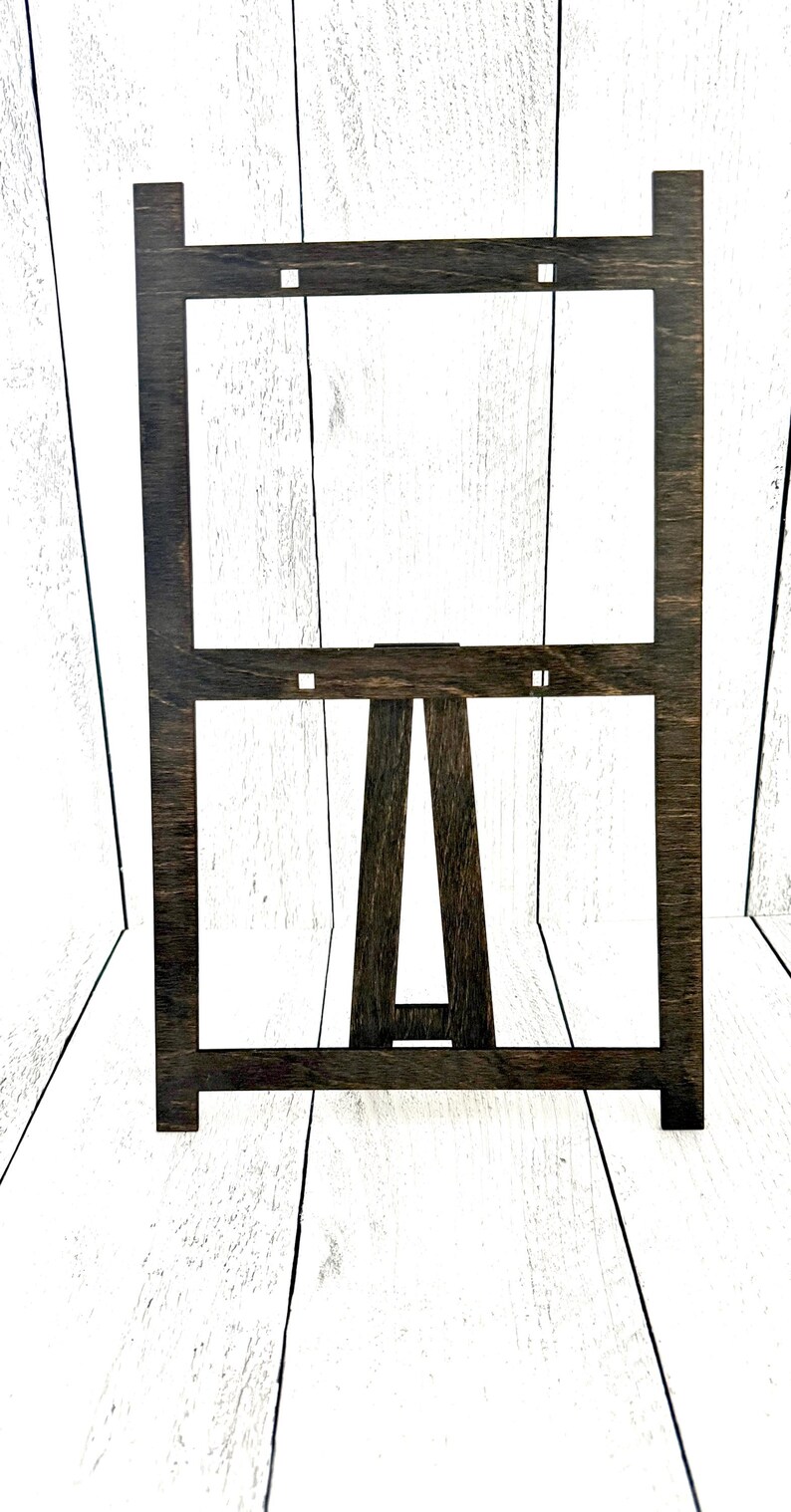 May include: A dark brown wooden easel stand with a rectangular frame. The easel is made of wood and has a simple design.