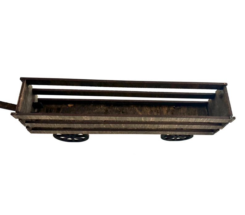 Puede incluir: Un vag&oacute;n de madera r&uacute;stico con una base rectangular y laterales de listones. El vag&oacute;n tiene dos ruedas de radios negras y un asa de metal. La madera tiene un aspecto gris-marr&oacute;n desgastado.