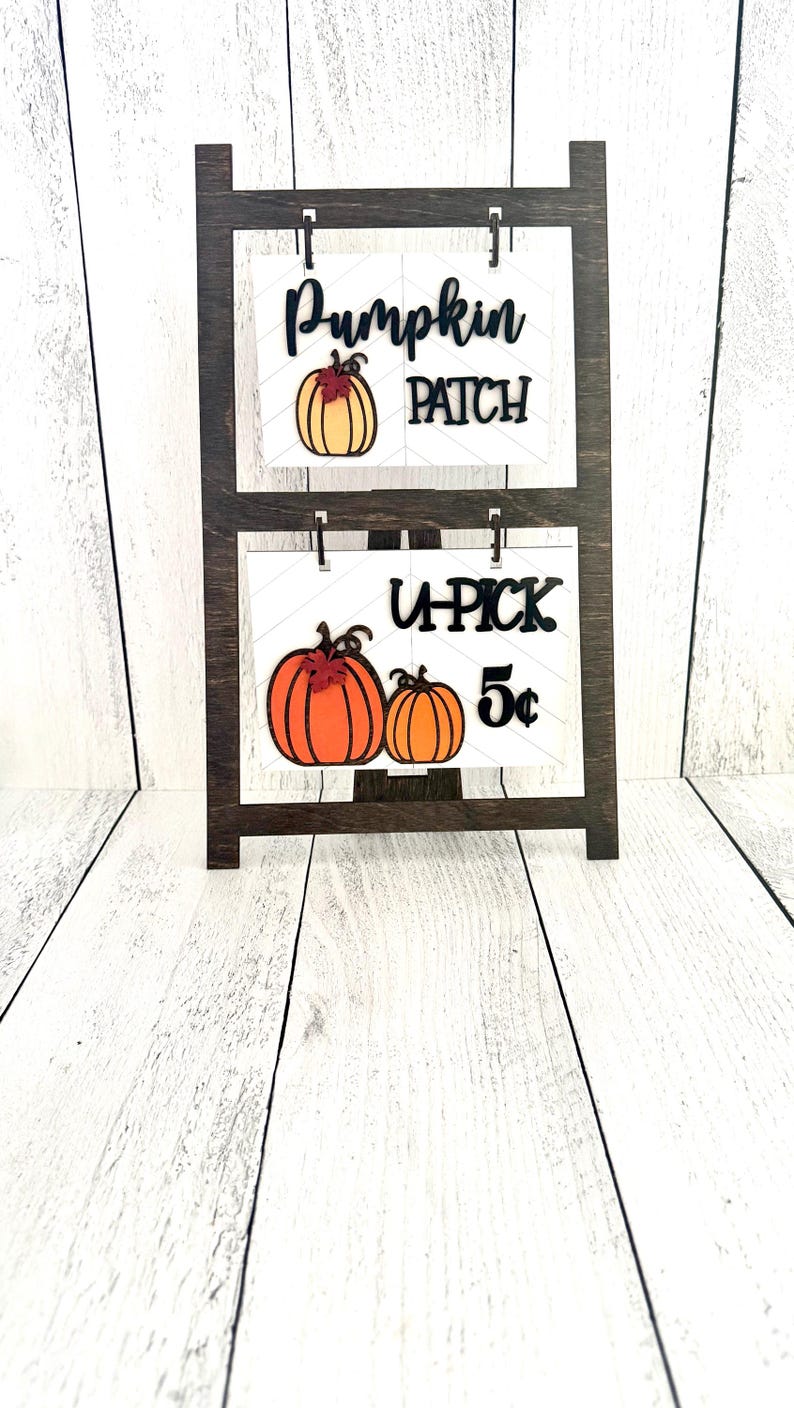 May include: A wooden stand with two signs. The top sign says "Pumpkin Patch" with a small orange pumpkin graphic. The bottom sign says "U-Pick 5&cent;" with two small orange pumpkins.