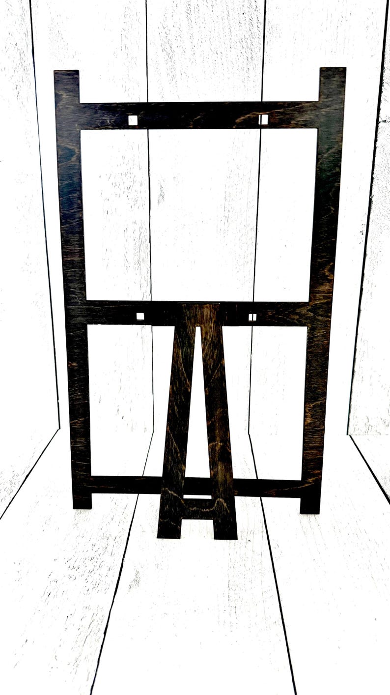 May include: A black wooden easel with a rectangular frame. The easel is made of wood and has a dark brown stain. The frame is made of wood and has a black stain.