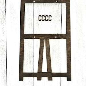 May include: A dark brown wooden easel with a rectangular frame. The frame has a white background and the text "CCCC" is printed in black.