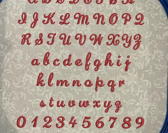 May include: A close-up of a white fabric with red embroidered letters and numbers. The letters include the alphabet in uppercase and lowercase, and the numbers 0 through 9.  There are also punctuation marks, including an exclamation point, quotation marks, an ampersand, an apostrophe, parentheses, a colon, a semicolon, a question mark, and a period.
